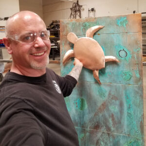 Metal artist Nate from Black Magic Metal Art shows installation of a turtle on a custom outdoor sculpture